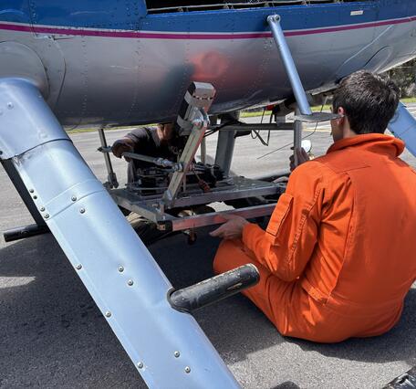 Color photograph of scientist mounting equipment at base of helicopter