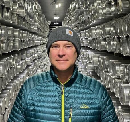 Image of man in blue jacket and gray hat standing between two rows of silver-wrapped ice cores. 