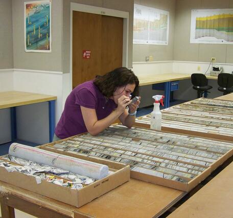 Woman in purple shirt looks at rock core through a hand lens