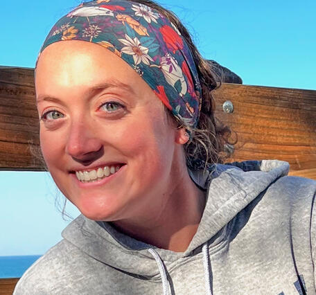 Woman wearing a hoodie and a head scarf sitting on a bench near a lake