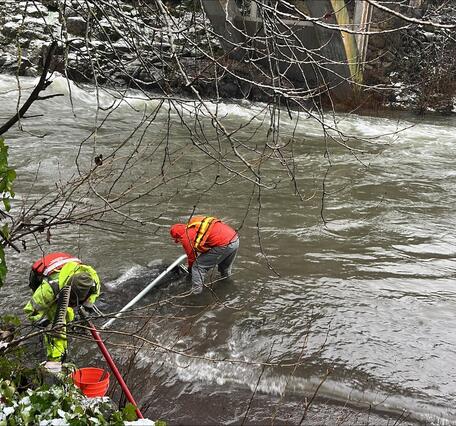 men in safety gear stand in rushing water fixing a pipe to the river bank