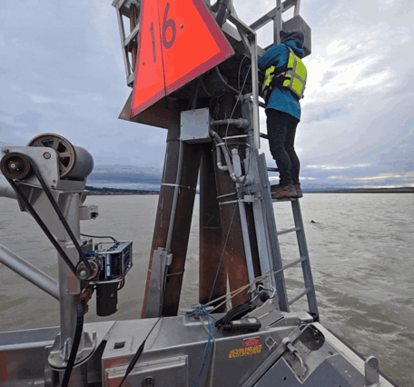 A technician climbs a steal dolphin to access gage equipment from a boat