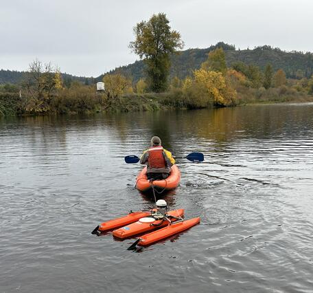 man paddles orange kayak towing an orange boat with flow measurement equipment 