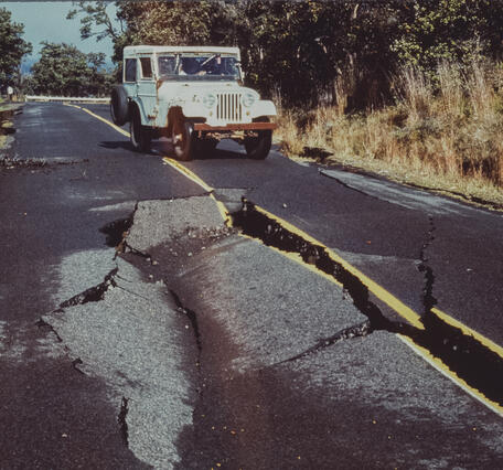 Color photograph of road cracks with vehicle in the background