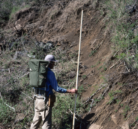 Color photograph of geologist in front of earthquake scarp