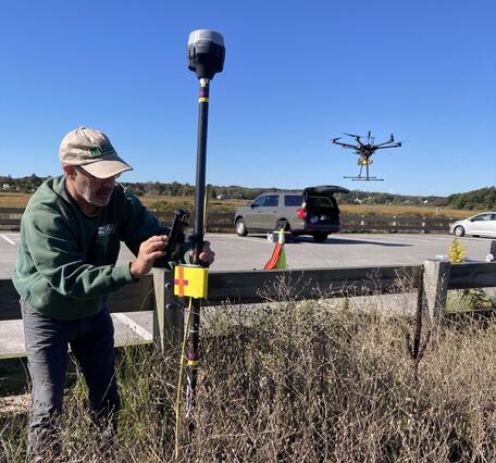 person using equipment in vegetation next to parking lot