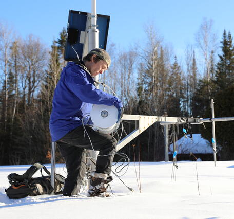 A man kneels down in the snow fixing metal equipment.