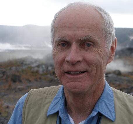 Color photograph of male scientist with steaming volcanic landscape in the background