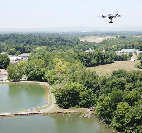 drone flying above reservoir located in a tree-covered landscape