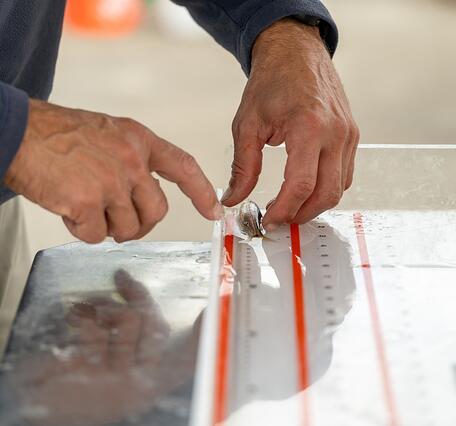 A male scientists measures a small silver fsh on a clear ruler with red markings. 