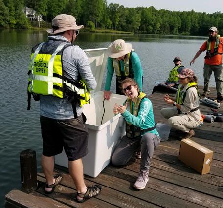 Six scientists in life vests gather and set up water quality monitoring equipment on a dock.