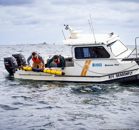 Two researchers on the R/V Dragonfly deploy a long yellow Autonomous Underwater Vehicle in Lake Michigan.