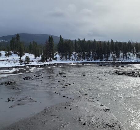 Klamath River flows through snow covered hills with sparse pine trees. Cloudy cold day