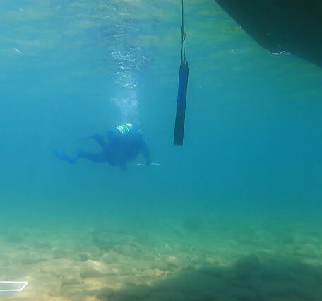 A diver approaching a scientific instrument hanging in the water beneath research vessel