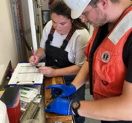 On a large research vessel, a researcher collecting a sample for glucose analysis and another recording the information