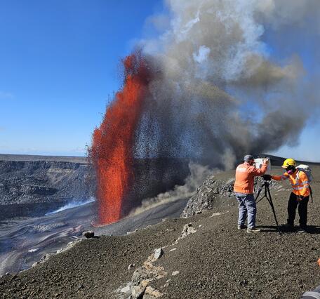Color photograph of scientists setting up monitoring equipment next to lava fountain