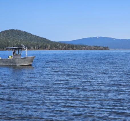 aluminum boat with a black USGS logo on vast blue lake waters. green forested hill in the background