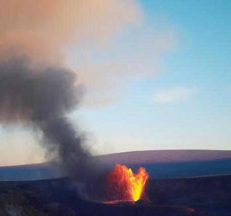 Color photograph of volcanic plume from eruption with mountain in the background
