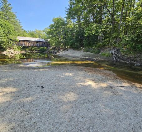 A dry riverbed with a covered bridge in the background.