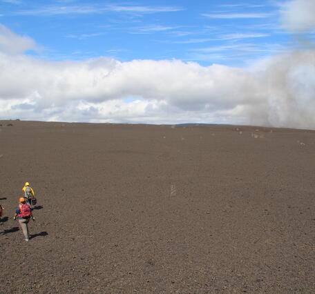 Color photograph of scientists walking across volcanic terrain to monitor eruption