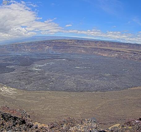 Desolate caldera with a steaming volcanic vent in the background under cloudy skies.