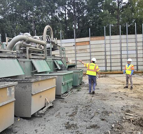 A USGS scientists leads a tour of a drilling site. He indicates where drilled sediments are deposited out of the shaker.