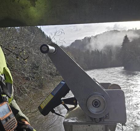 A man suspended above the river operates an aluminum crane used to lower measurement equipment into the water