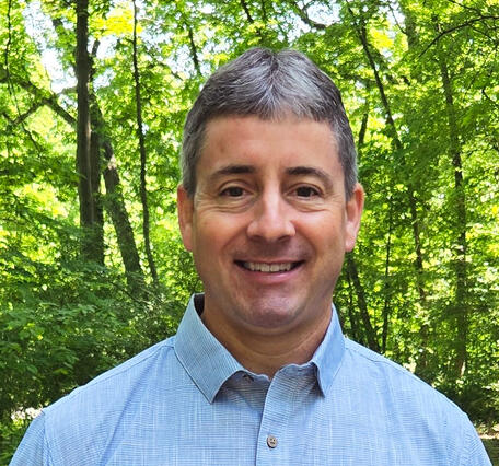 A researcher smiling standing in front of woods
