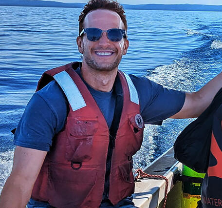 Researcher wearing a life vest sitting on a boat gunwale.
