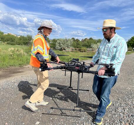 Two pilots carry drone aircraft on gravelly road
