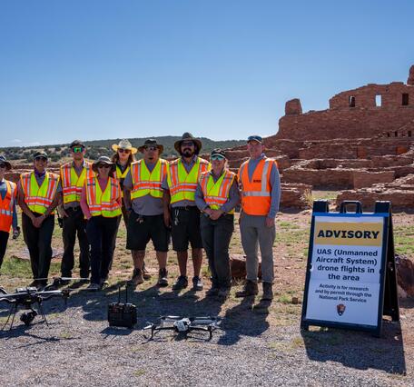 USGS and National Park workers pose with drone in front of stone structure at Abó Ruins
