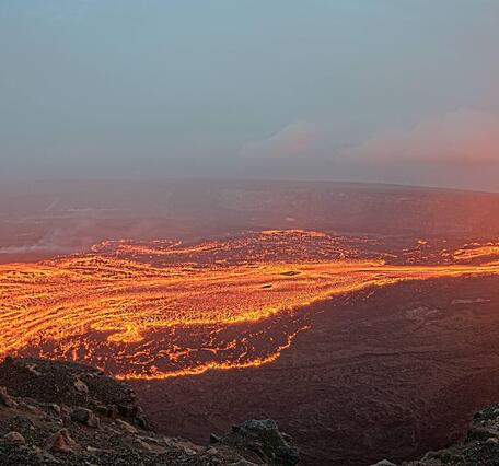 Color photograph of lava fountain feeding lava flows on the floor of a crater