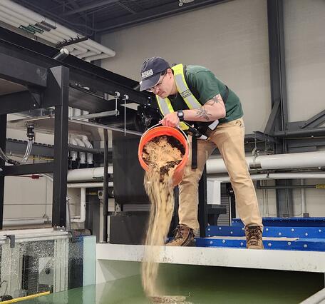 A Physical Scientist introducing sediment into the HIF tilting flume.