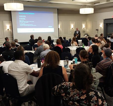 Conference room full of people sitting at tables watching presentation