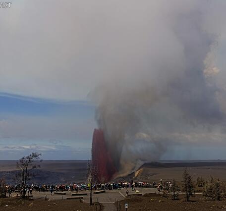 Color photograph of lava fountain erupting with visitors viewing in the foreground