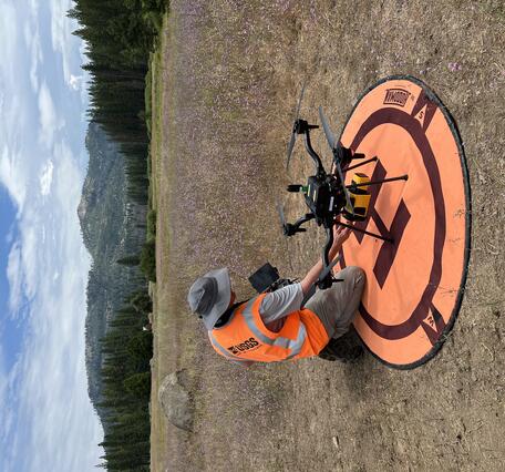 UAS pilot readying craft that sits on landing pad situated in a mountain clearing