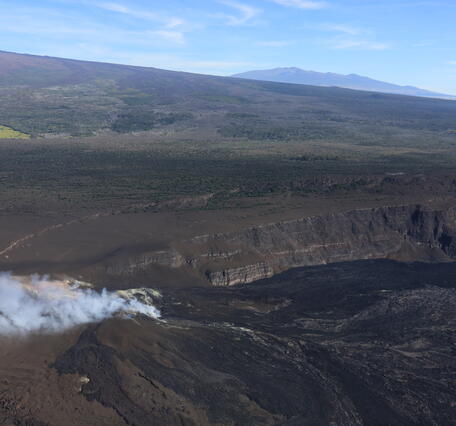 Color photograph of crater at summit of volcano with another volcano in background