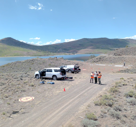 UAS personnel stand next to their vehicles as they control drone above reservoir