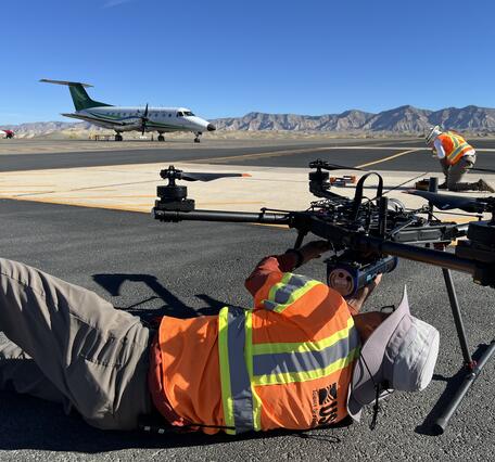 Drone operator laying on airstrip, securing sensors to the underside of UAS craft.