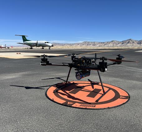 UAS sitting on landing pad at the Grand Junction Regional Airport, with small airplane in background.