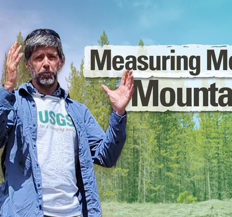 Thumbnail image of a man standing outside holding up his hands and speaking in front of a forest