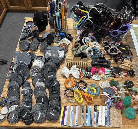 camera lens caps, hair accessories, pacifiers, sunglasses, and hotel key cards laid out on a wooden table