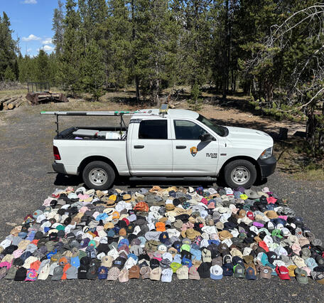 A white pickup truck is parked in front of an array of hundreds of hats of various colors laid out on the ground