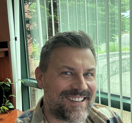 staff profile showing a man smiling in front of a window