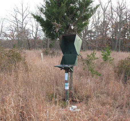 A well standpipe with an open access box on top stands in the middle of a grassy field