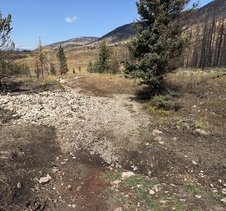 a bile of rocks and mud partially covering a dirt road with mountains visible in the background