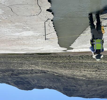 technician stands in ankle deep silty water running through the dry saline lakebed on a sunny spring day