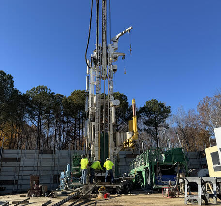 Drill rig lowering extensometer pipe into a borehole.