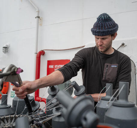 A person in a hat works on Niskin bottles attached to a CTD