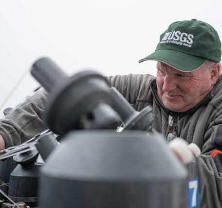A person in a USGS hat sets Niskin bottles on a CTD